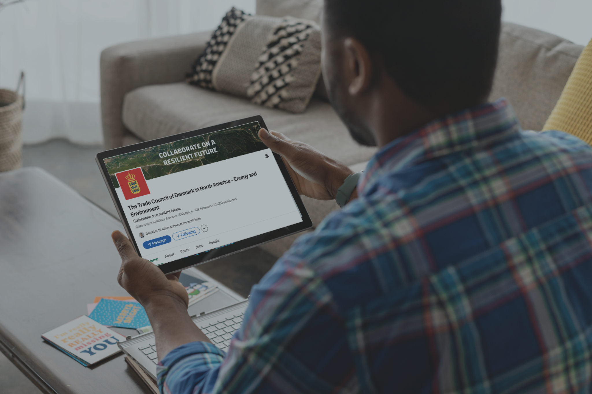 Photo of man holding iPad in a living room with the Trade Council of Denmark in North America's LinkedIn on the screen.